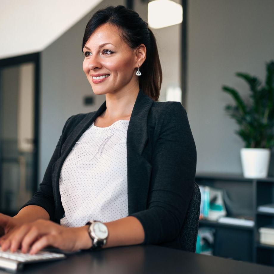 A woman working at a desktop monitor in a warm, low-lit office.